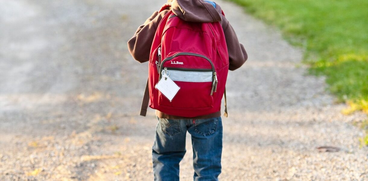 Enfant de dos avec son cartable rouge marchant sur un chemin