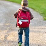 Enfant de dos avec son cartable rouge marchant sur un chemin