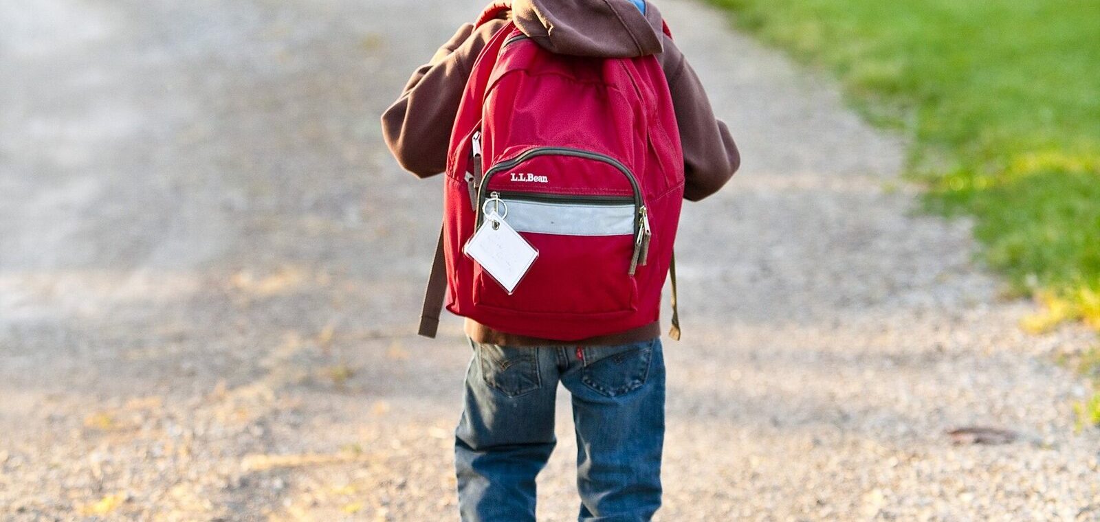 Enfant de dos avec son cartable rouge marchant sur un chemin