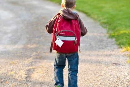 Enfant de dos avec son cartable rouge marchant sur un chemin