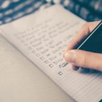 Main qui coche une liste de tâches dans un carnet à petits carreaux