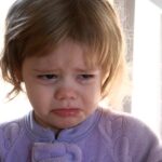 Petite fille en pleurs, le visage crispé, vêtue d'un gilet violet