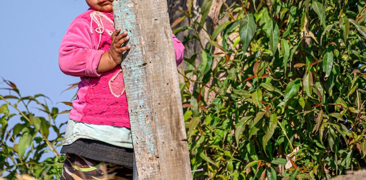 Petite fille qui se cache à moitié derrière un poteau en bois