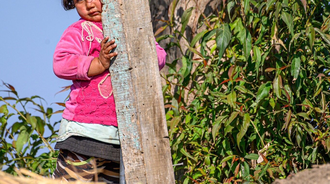 Petite fille qui se cache à moitié derrière un poteau en bois