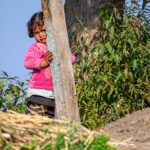 Petite fille qui se cache à moitié derrière un poteau en bois