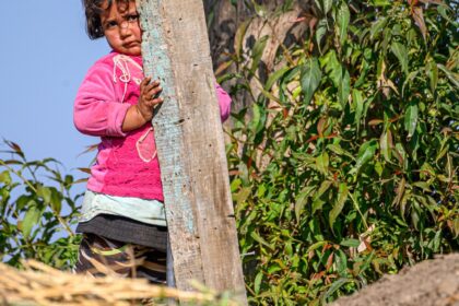 Petite fille qui se cache à moitié derrière un poteau en bois