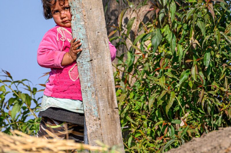 Petite fille qui se cache à moitié derrière un poteau en bois