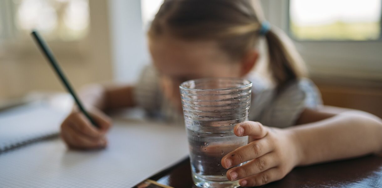 Enfant qui écrit dans un cahier avec un verre d'eau au premier plan