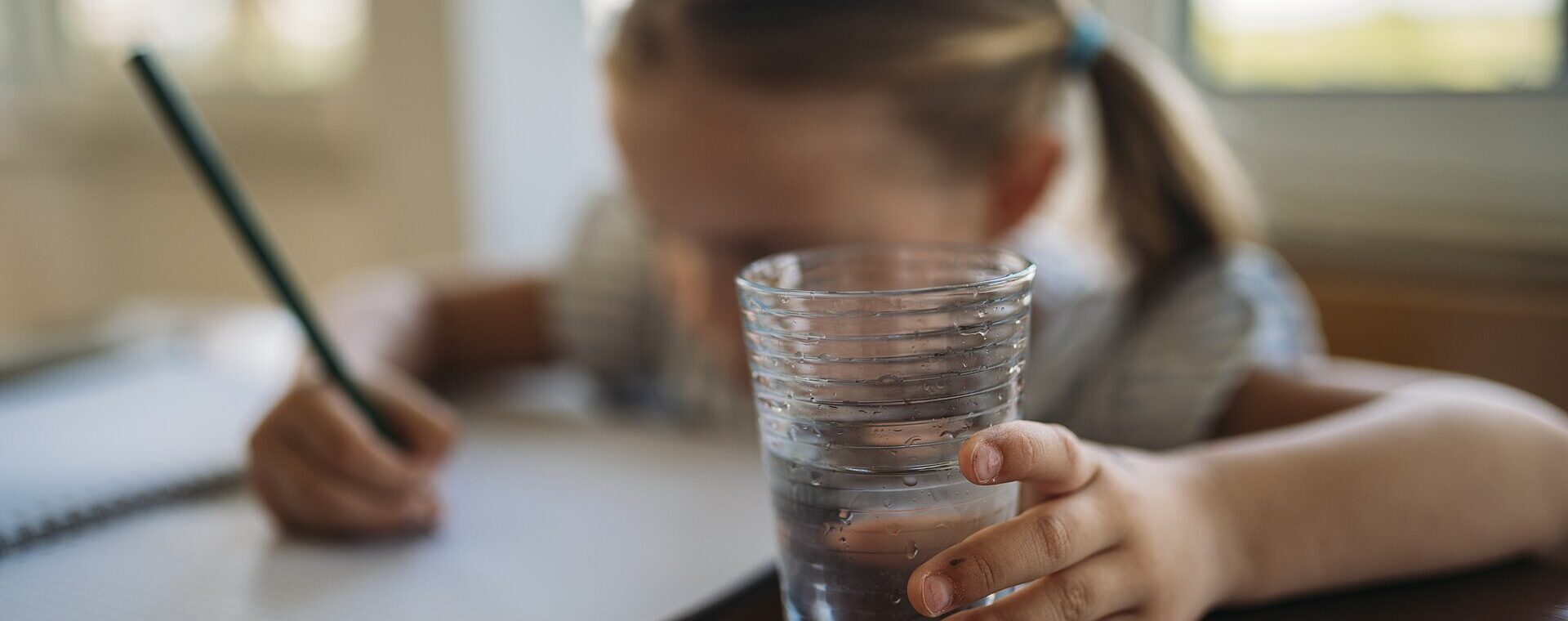 Enfant qui écrit dans un cahier avec un verre d'eau au premier plan